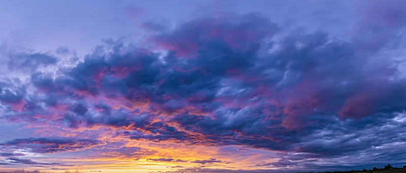 Panoramic view of a dramatic sunset sky filled with cumulus clouds over a rural horizon