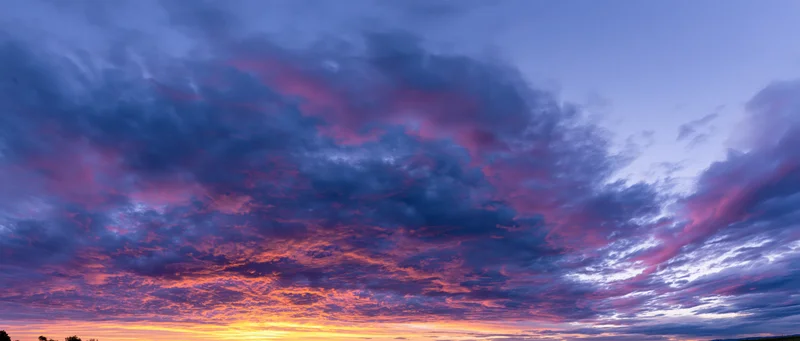 Panoramic sky at sunset with dramatic cumulus clouds and vibrant colors across the horizon