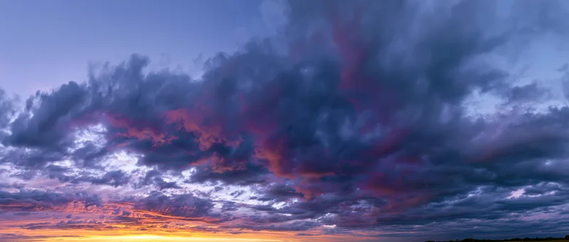 Panoramic view of dramatic cumulus clouds at sunset over a distant horizon