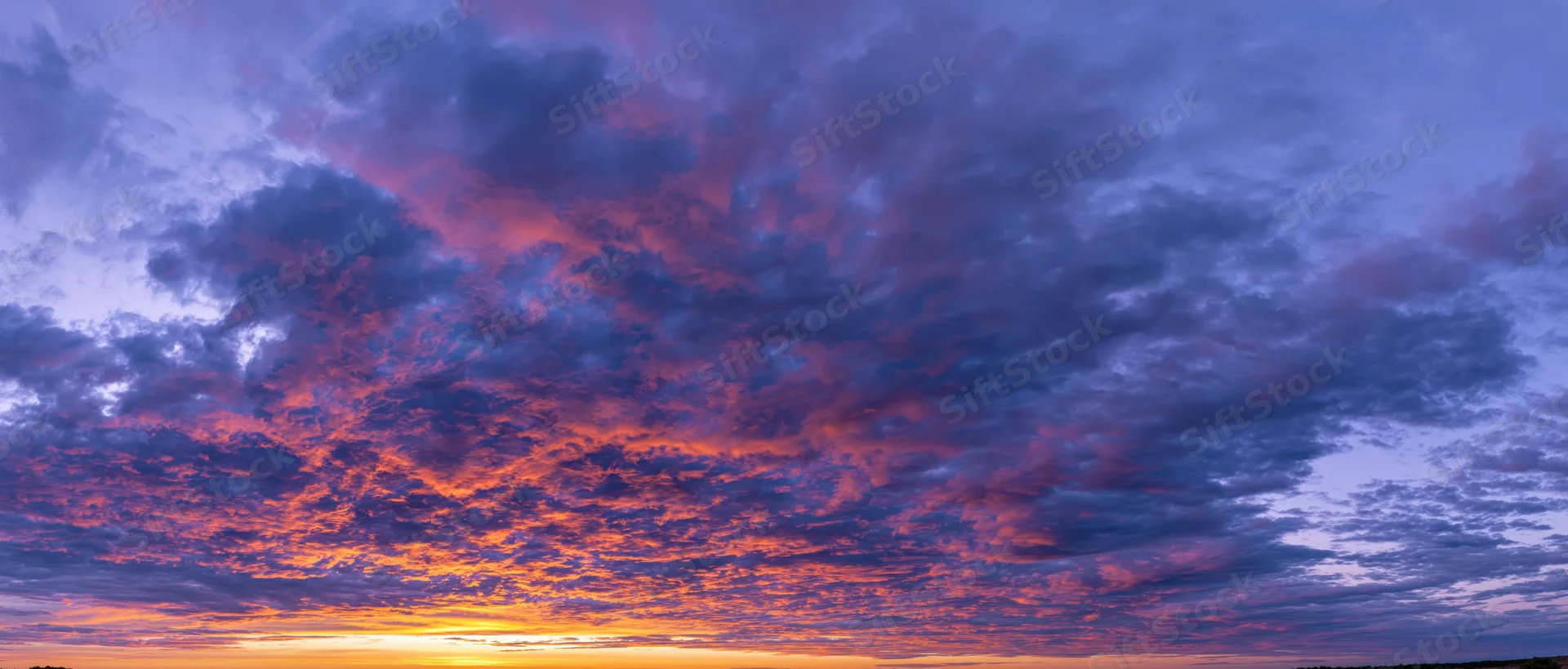 Panoramic sky at sunset with dramatic cumulus clouds and vibrant orange purple hues above the horizon