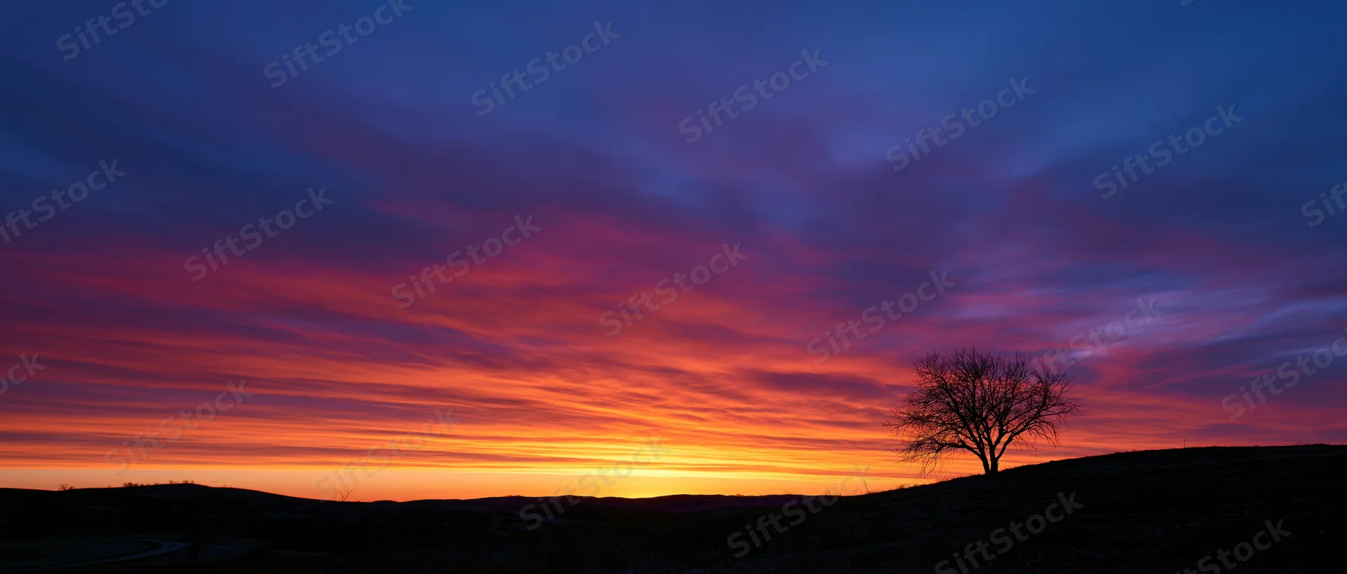 Panoramic sunset sky over rolling hills with dramatic clouds and a silhouetted tree