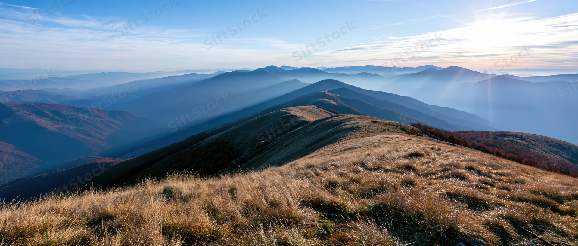Panoramic view from mountain summit overlooking layered valleys and ridges under sunrise light
