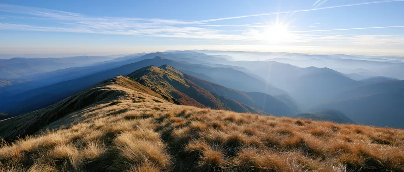 Panoramic view from mountain summit overlooking layered valleys and ridges at sunrise
