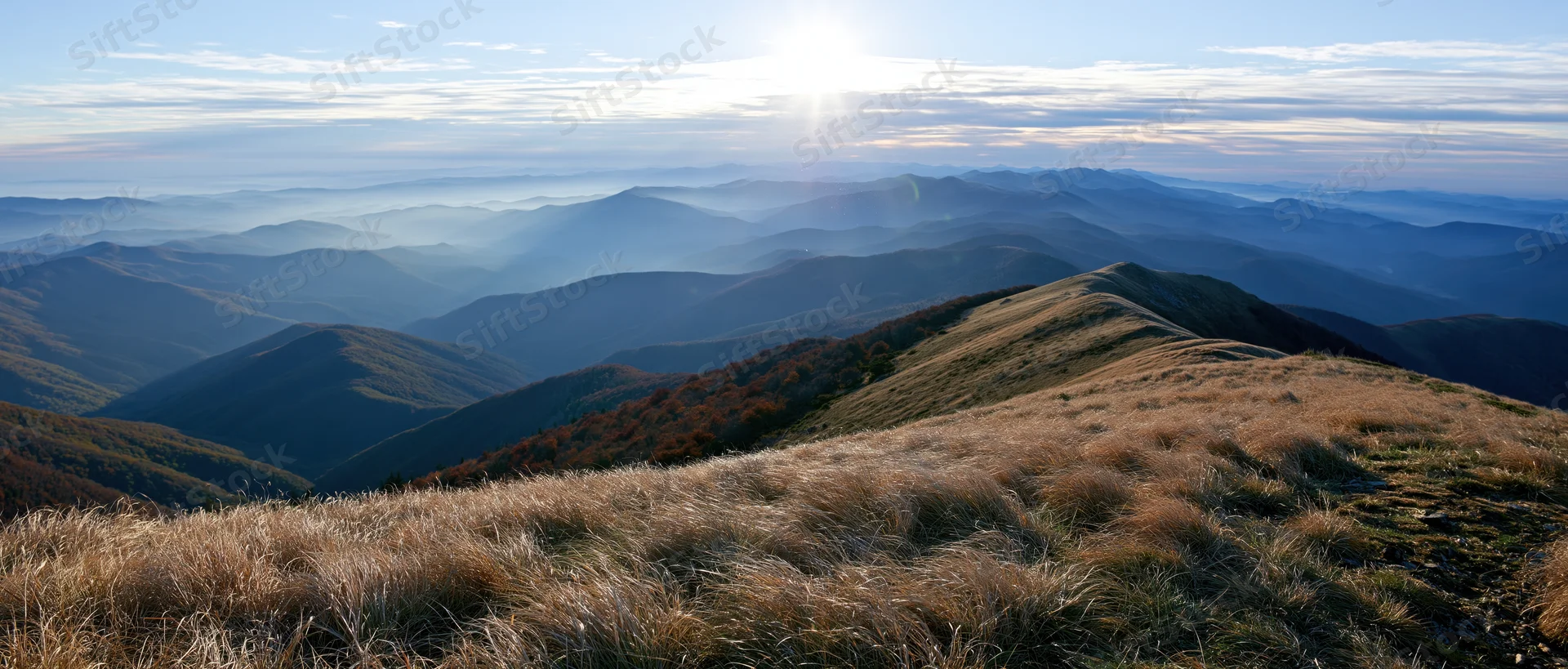 Panoramic view from mountain summit overlooking layered valleys and ridges under sunrise sky
