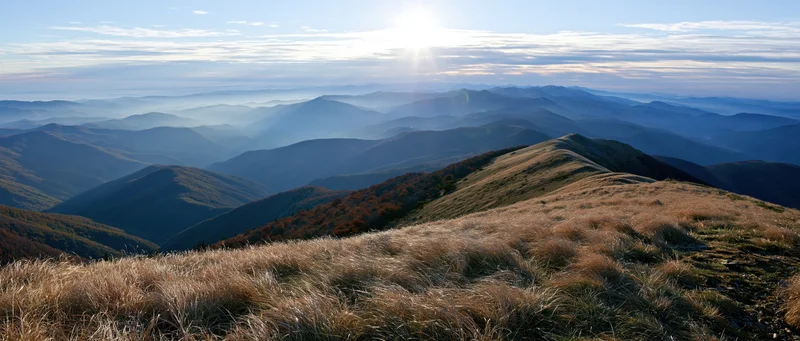 Panoramic view from mountain summit overlooking layered valleys and ridges under sunrise sky