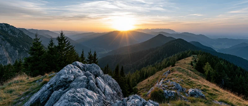 Panoramic view from rocky alpine summit at golden hour overlooking forested valleys and distant peaks