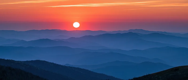 Panoramic view of layered Appalachian mountain ridges at sunset with orange sky and blue valleys
