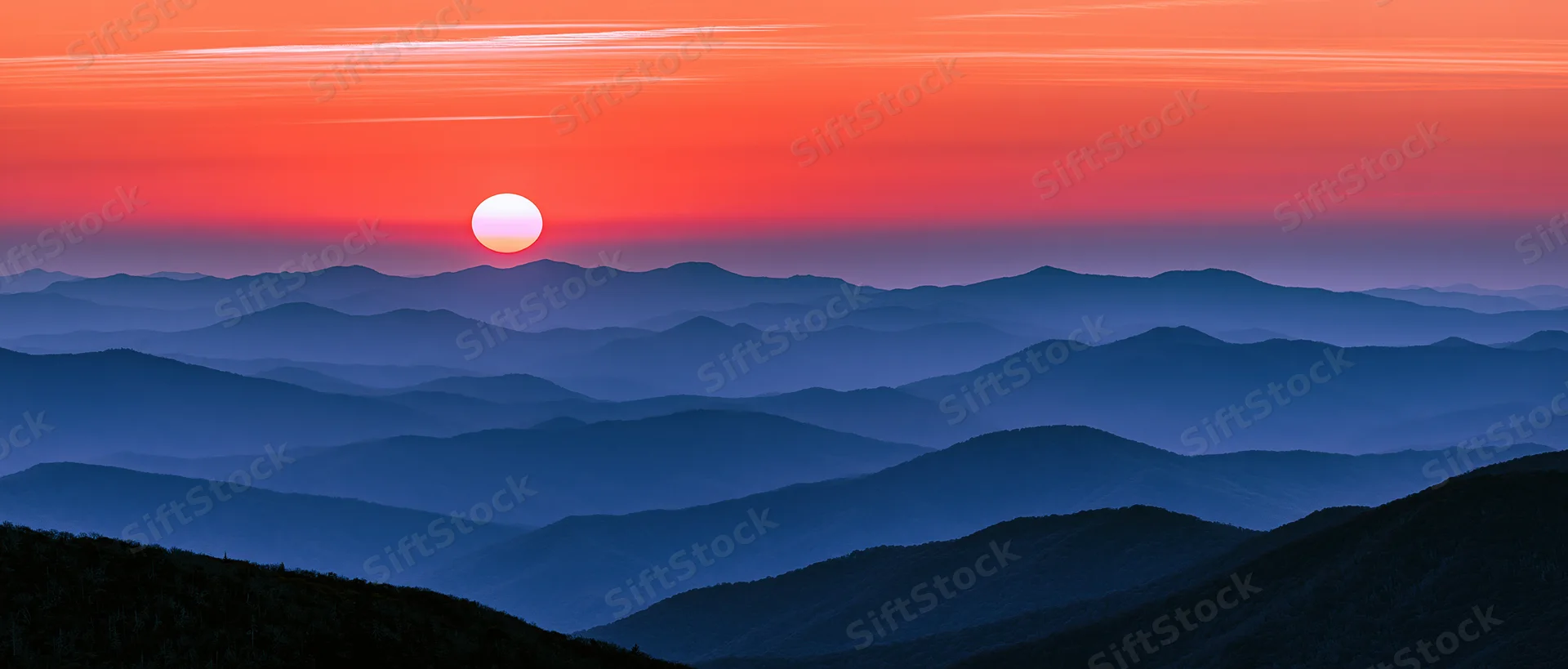 Layered mountain ridges under a vibrant orange and blue sunset sky