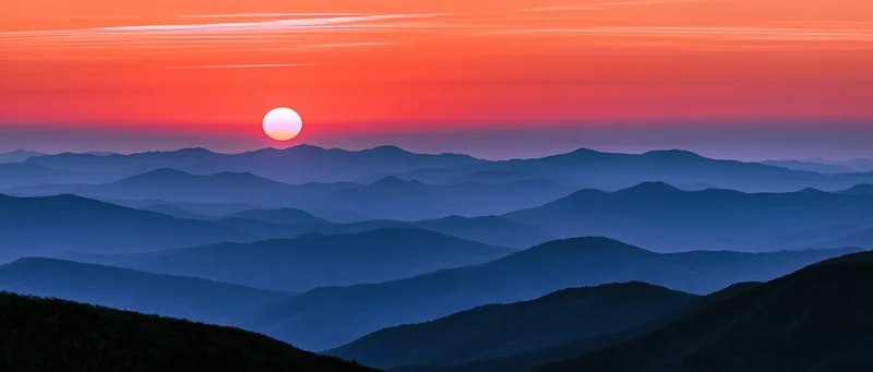 Layered mountain ridges under a vibrant orange and blue sunset sky