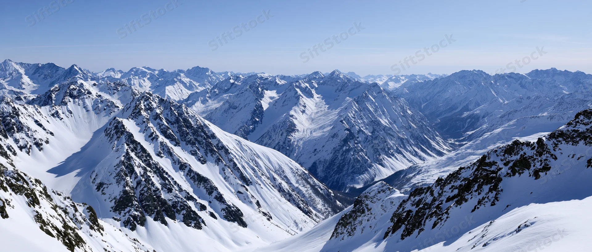 Panoramic view of snow-covered alpine mountain peaks and valleys under clear blue sky
