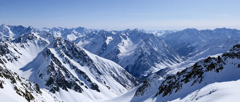 Panoramic view of snow-covered alpine mountain peaks and valleys under clear blue sky