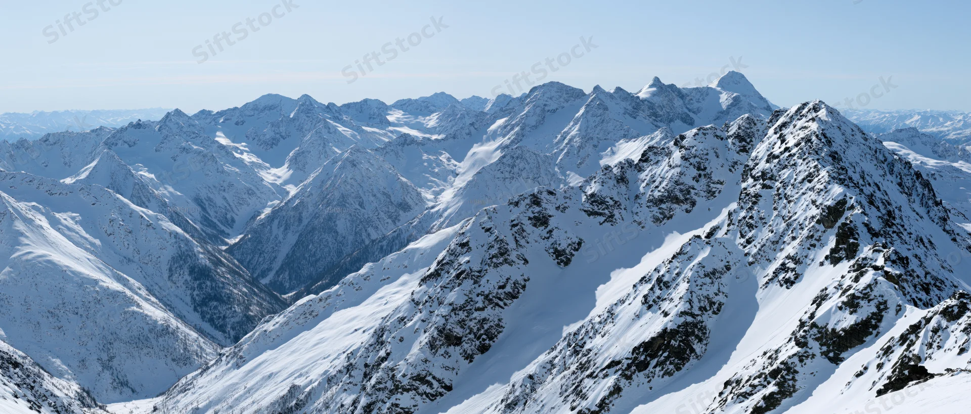 Panoramic view of snow-covered alpine mountain peaks and valleys under clear sky