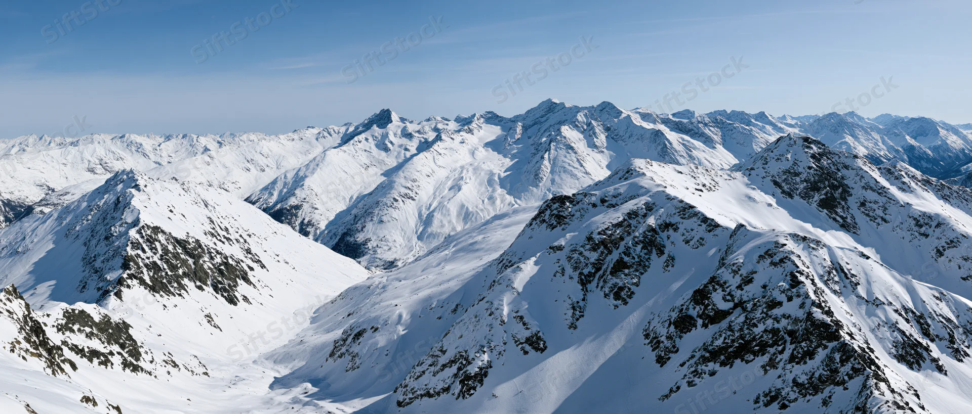 Panoramic view of snow-covered alpine mountain peaks under clear blue sky