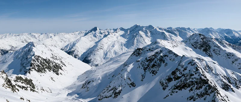 Panoramic view of snow-covered alpine mountain peaks under clear blue sky