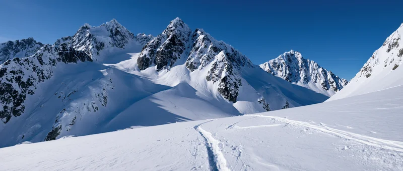 Snow-covered alpine peaks rising above a snowy valley with ski tracks leading toward the ridges under a clear blue sky