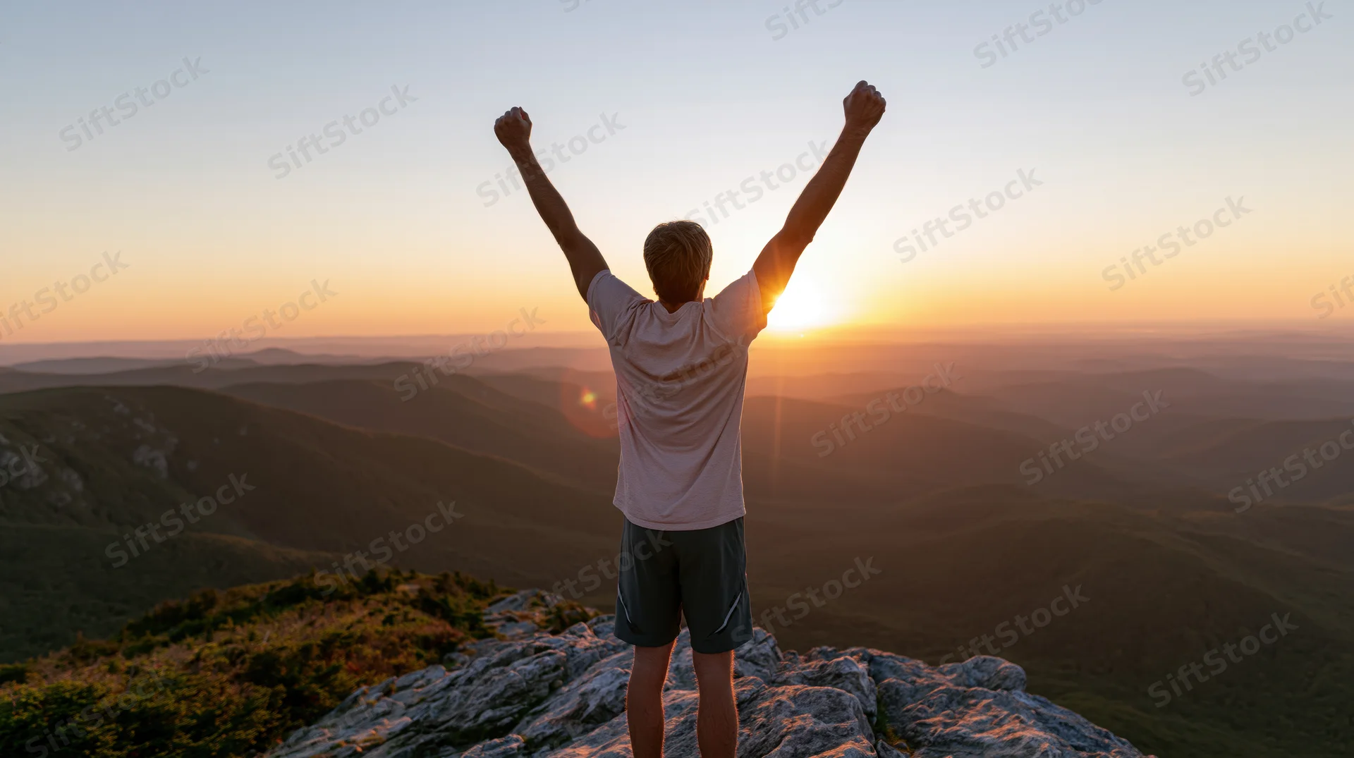 Man standing on mountain summit with arms raised at sunrise