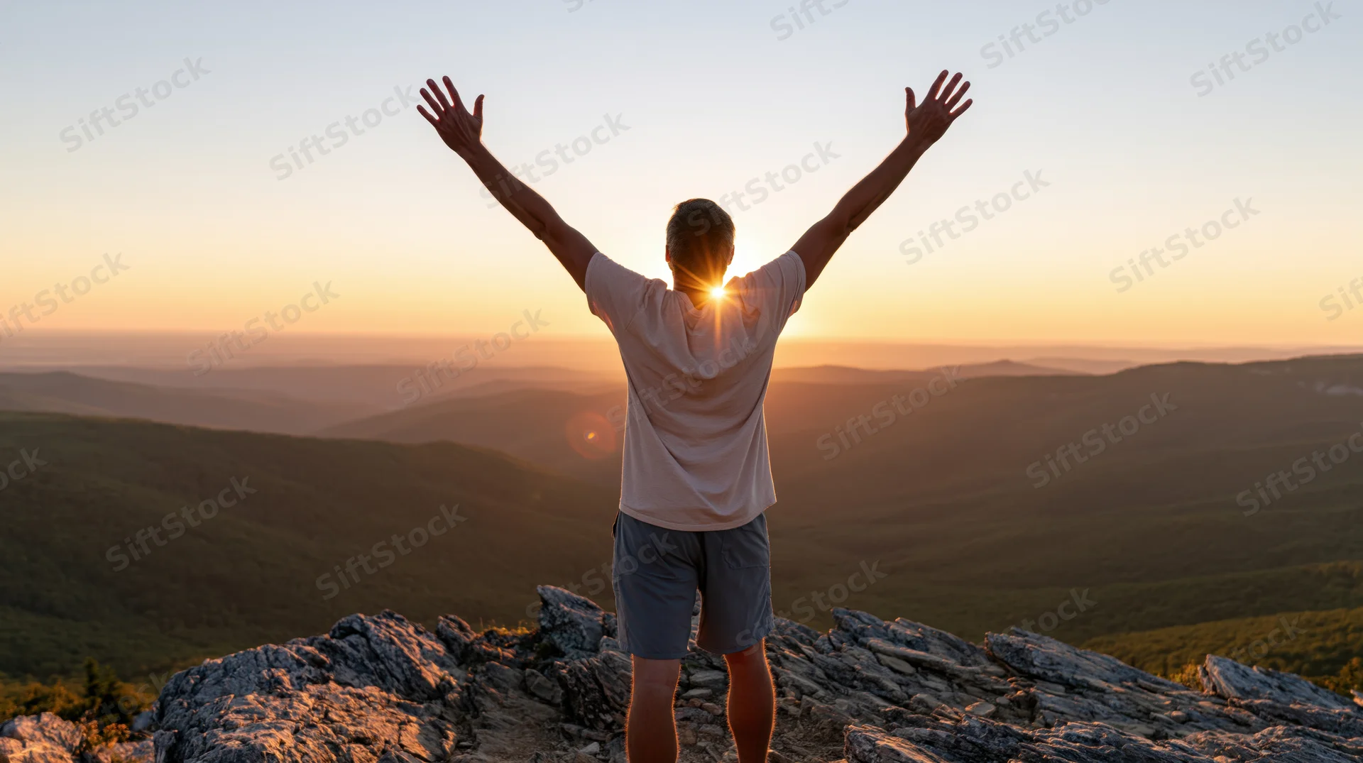 Man standing on rocky mountain summit with arms raised at sunset