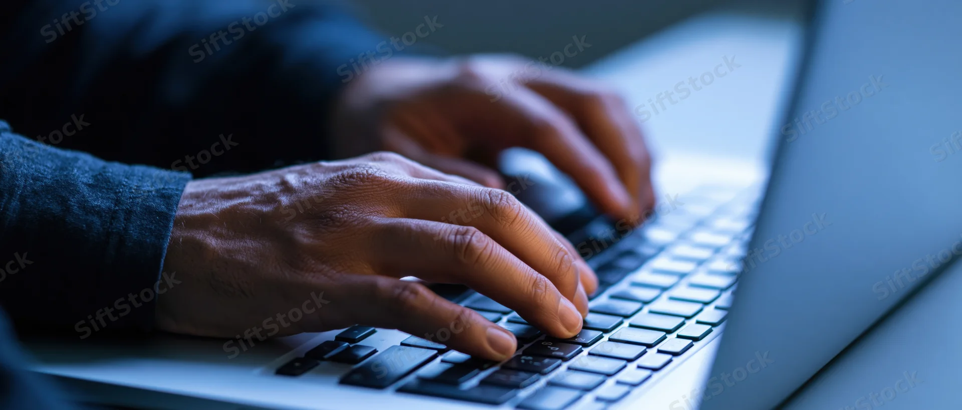 Hands typing on a laptop keyboard at a desk with a mouse nearby