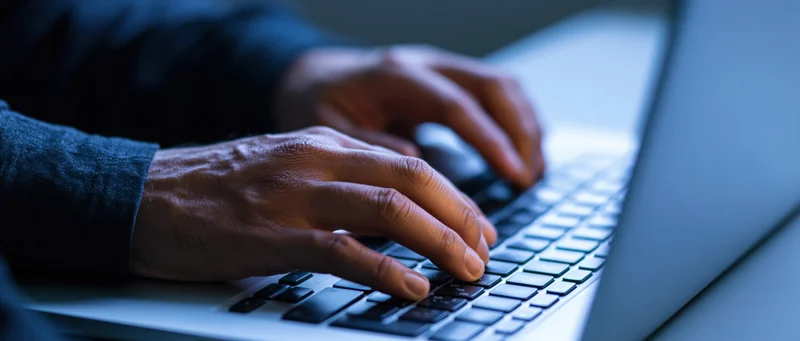 Hands typing on a laptop keyboard at a desk with a mouse nearby