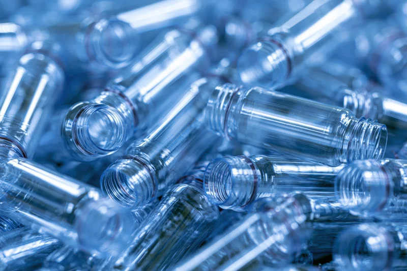 Heap of clear plastic bottle preforms scattered in industrial setting