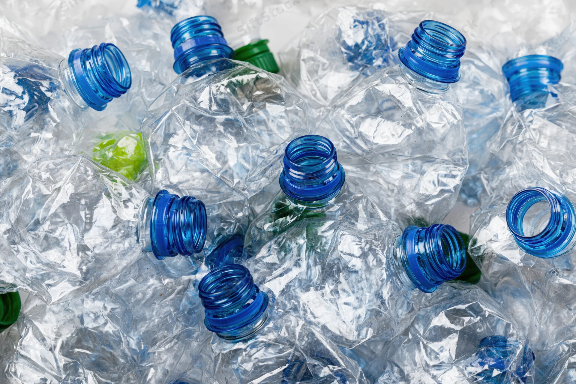 Crushed clear plastic water bottles with blue caps piled together