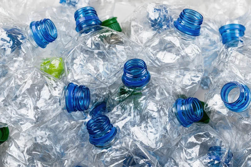Crushed clear plastic water bottles with blue caps piled together