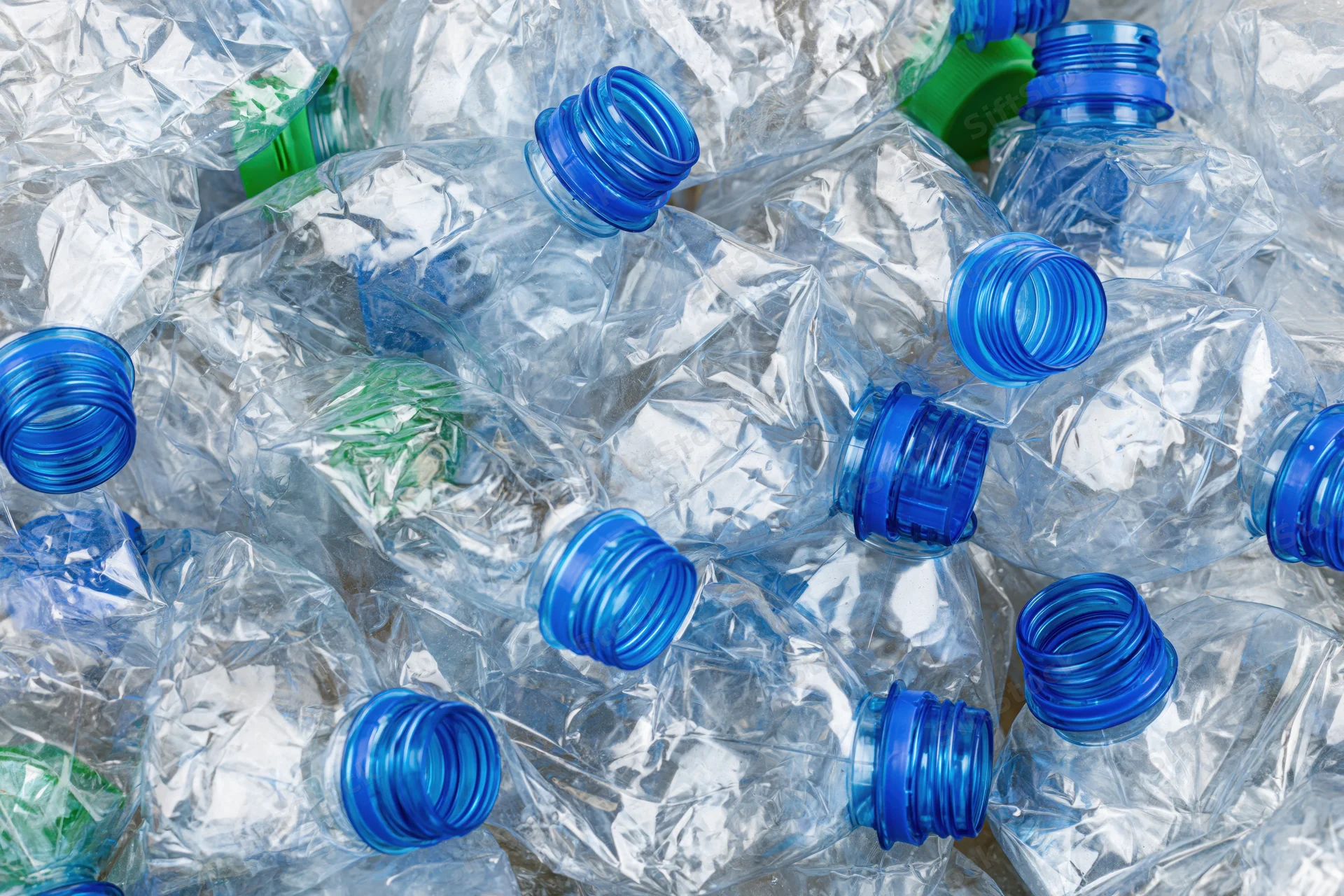 Crushed clear plastic water bottles piled together with blue and green caps