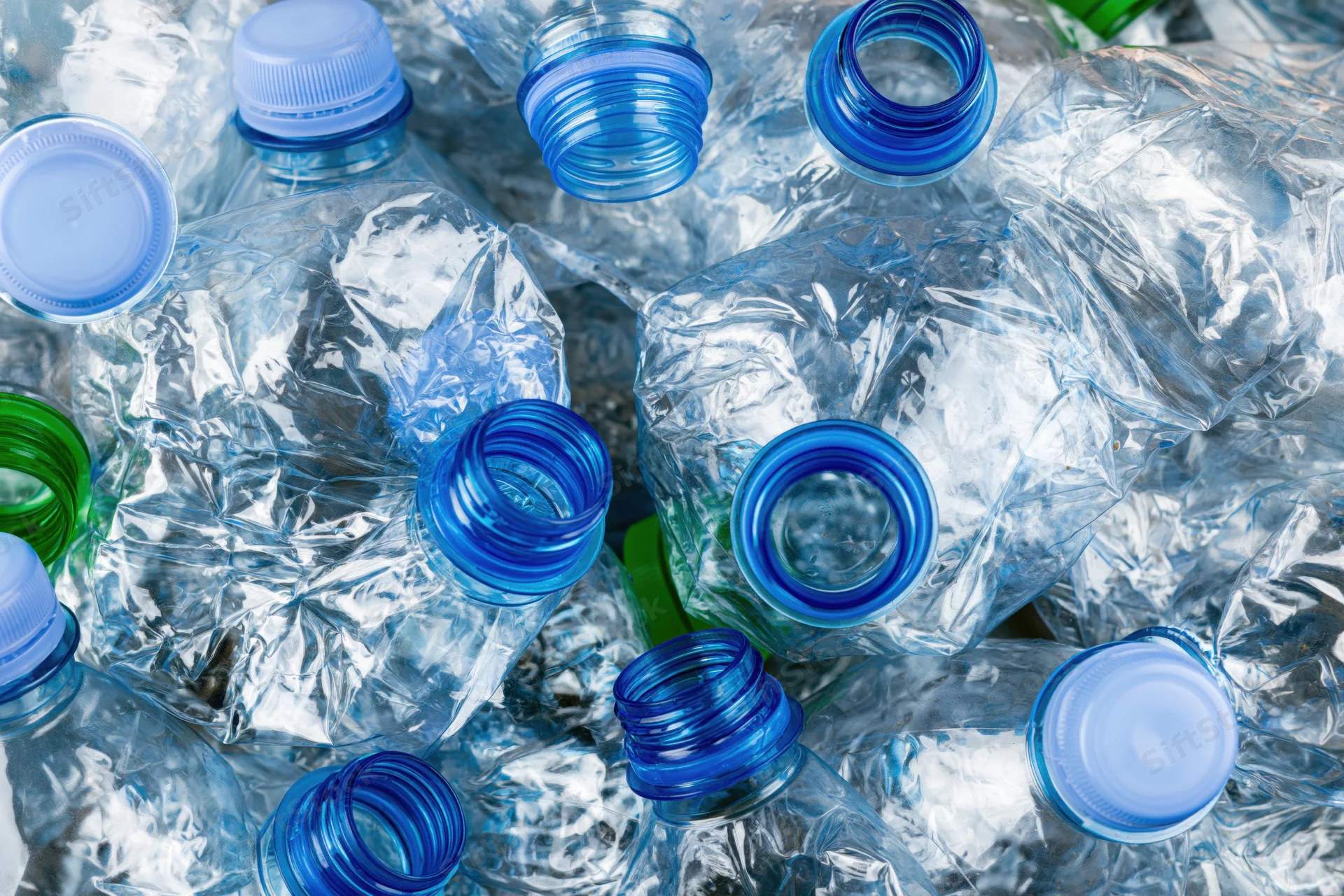 Crushed clear plastic water bottles with blue caps piled together