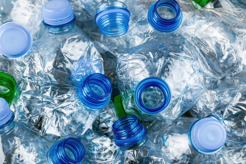 Crushed clear plastic water bottles with blue caps piled together