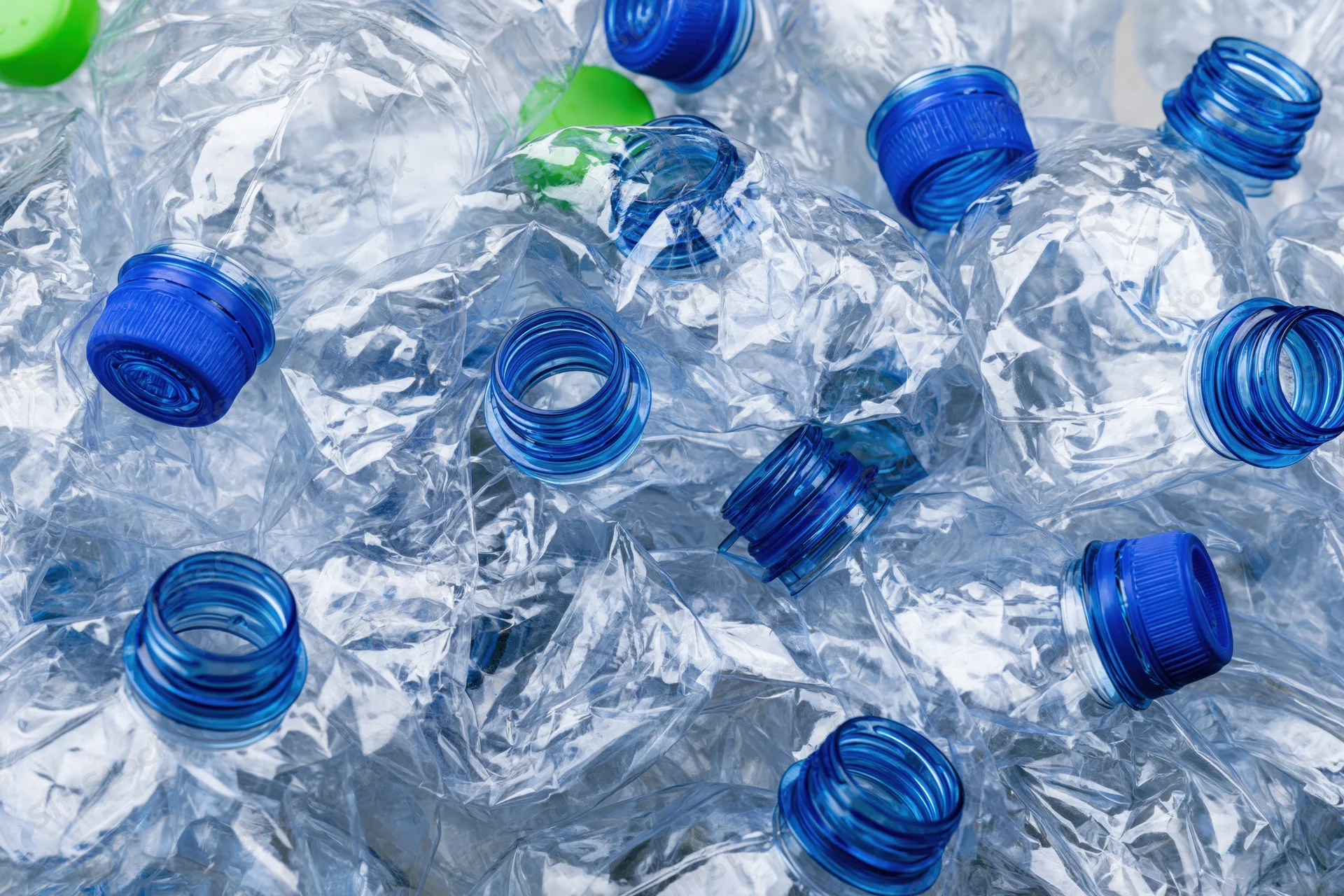 Crushed clear plastic water bottles with blue caps piled together