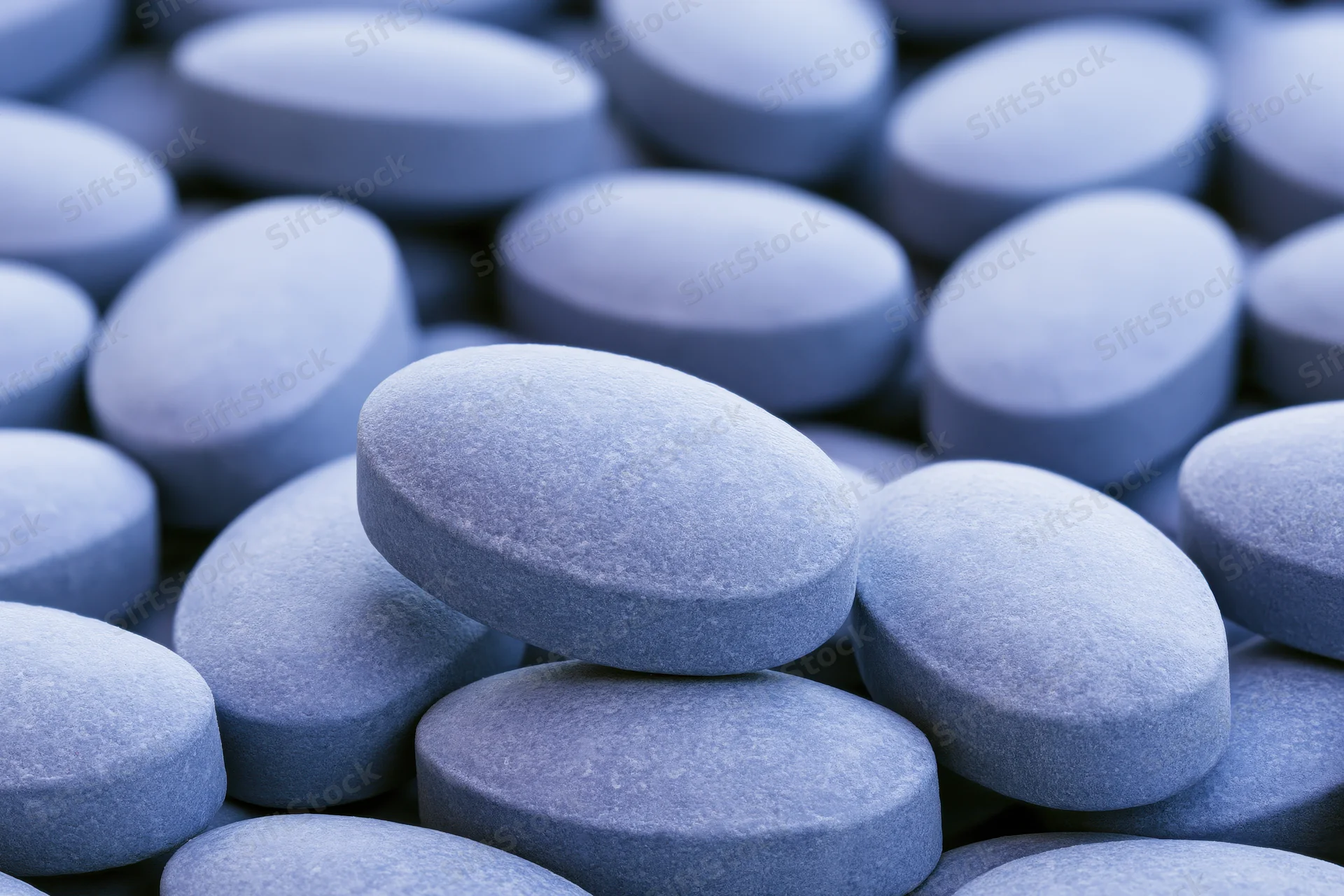 Closeup of oval blue coated tablets piled together filling the frame