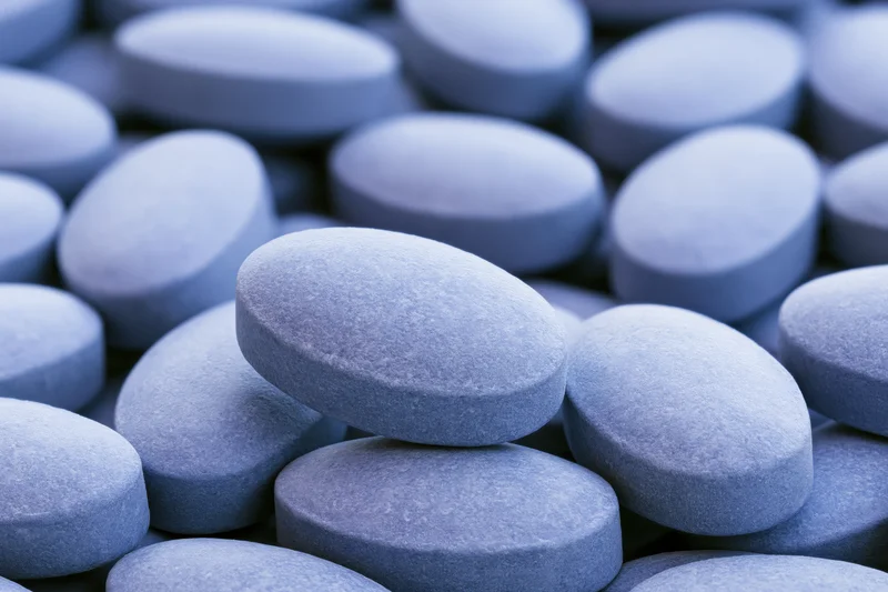 Closeup of oval blue coated tablets piled together filling the frame