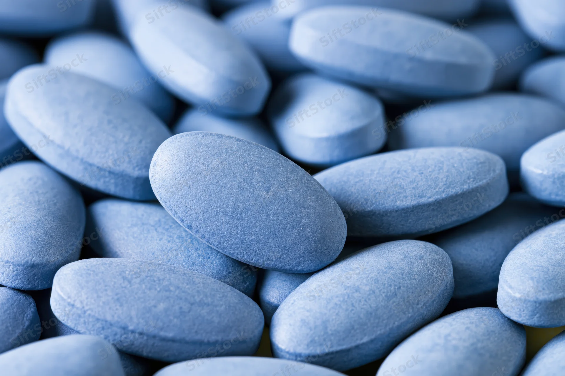 Close-up of oval blue coated tablets piled together filling the frame