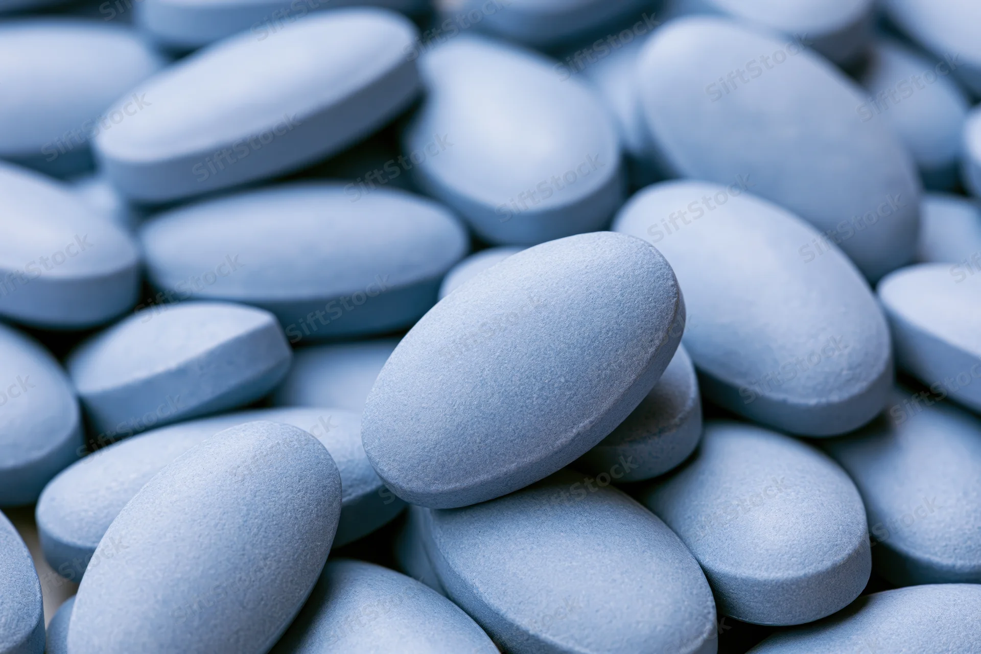 Closeup of oval blue coated tablets piled together filling the frame