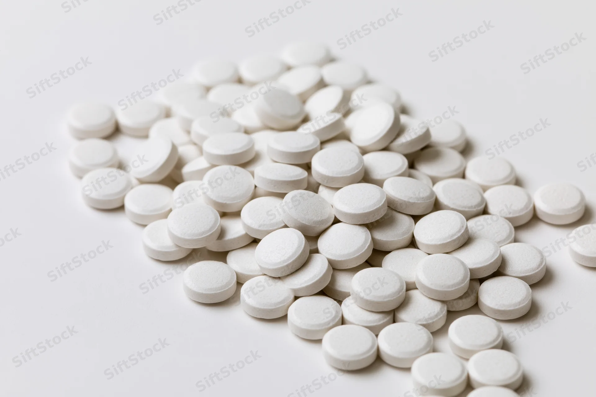 Scattered white round tablets piled on a plain white surface