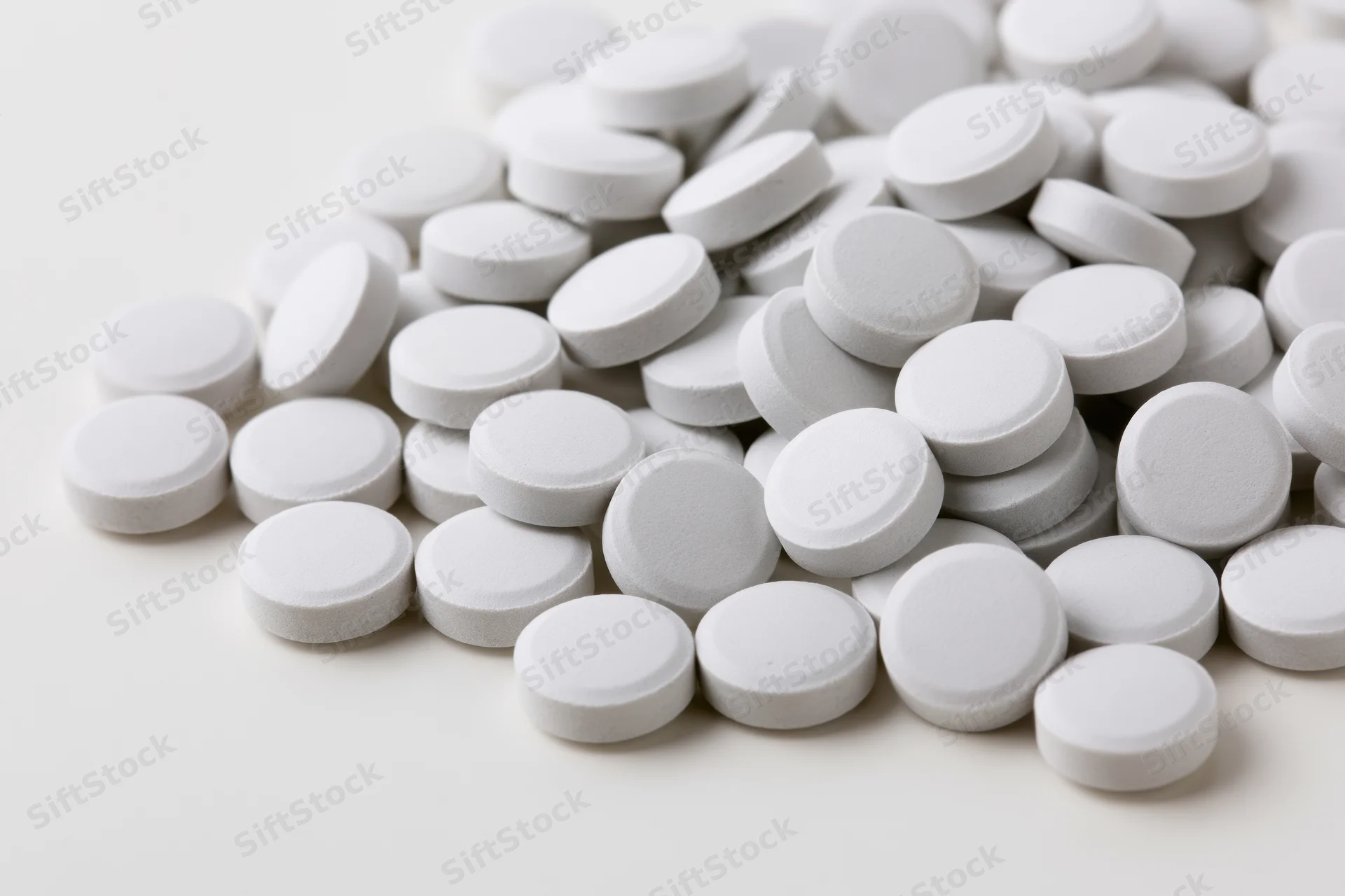 Pile of small white round tablets scattered on a plain surface
