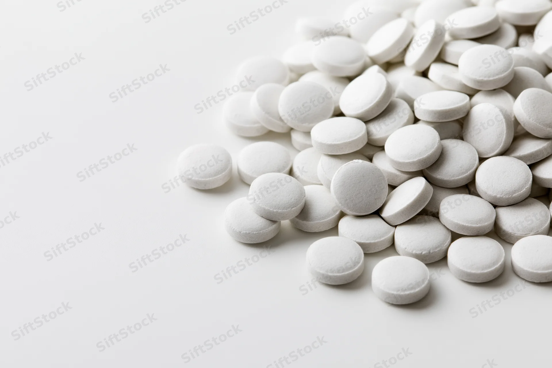 Pile of small white round tablets scattered on a white surface
