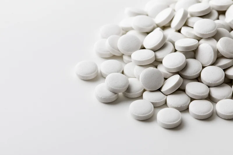 Pile of small white round tablets scattered on a white surface
