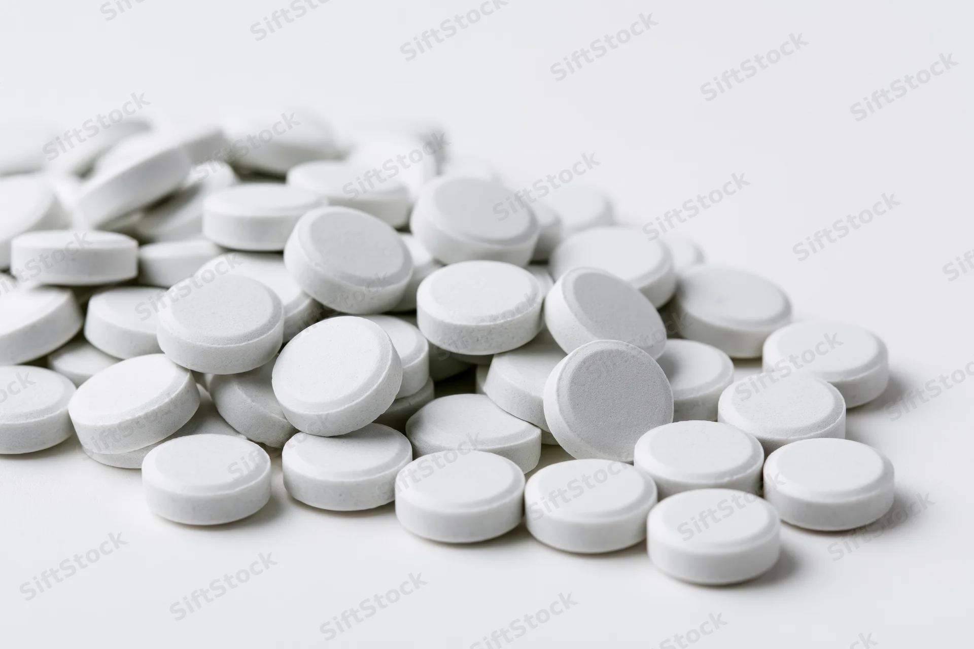 Pile of small white round tablets scattered on a plain white surface