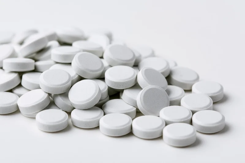 Pile of small white round tablets scattered on a plain white surface