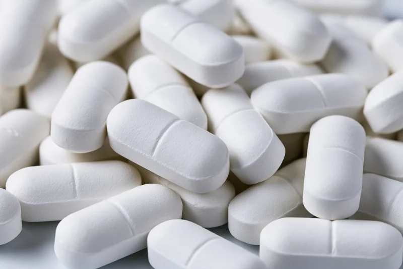 Pile of white oval pharmaceutical tablets scattered loosely on a light surface