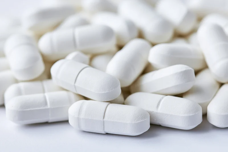 White oval pharmaceutical tablets scattered loosely on a plain surface