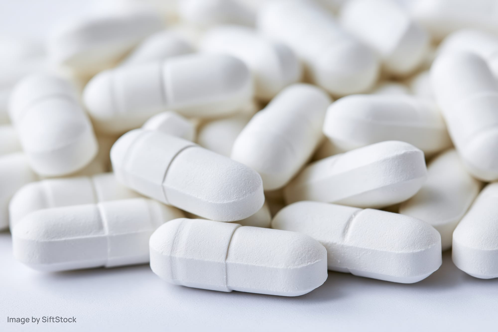 White oval pharmaceutical tablets scattered loosely on a plain surface