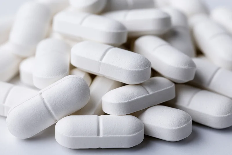 Pile of white oval pharmaceutical tablets scattered loosely on a plain surface