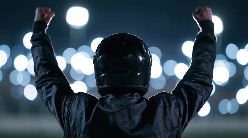 Racing driver in black suit and helmet raising arms in victory at night race track