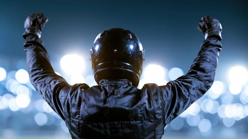 Racing driver with arms raised in victory at night on a lit racetrack