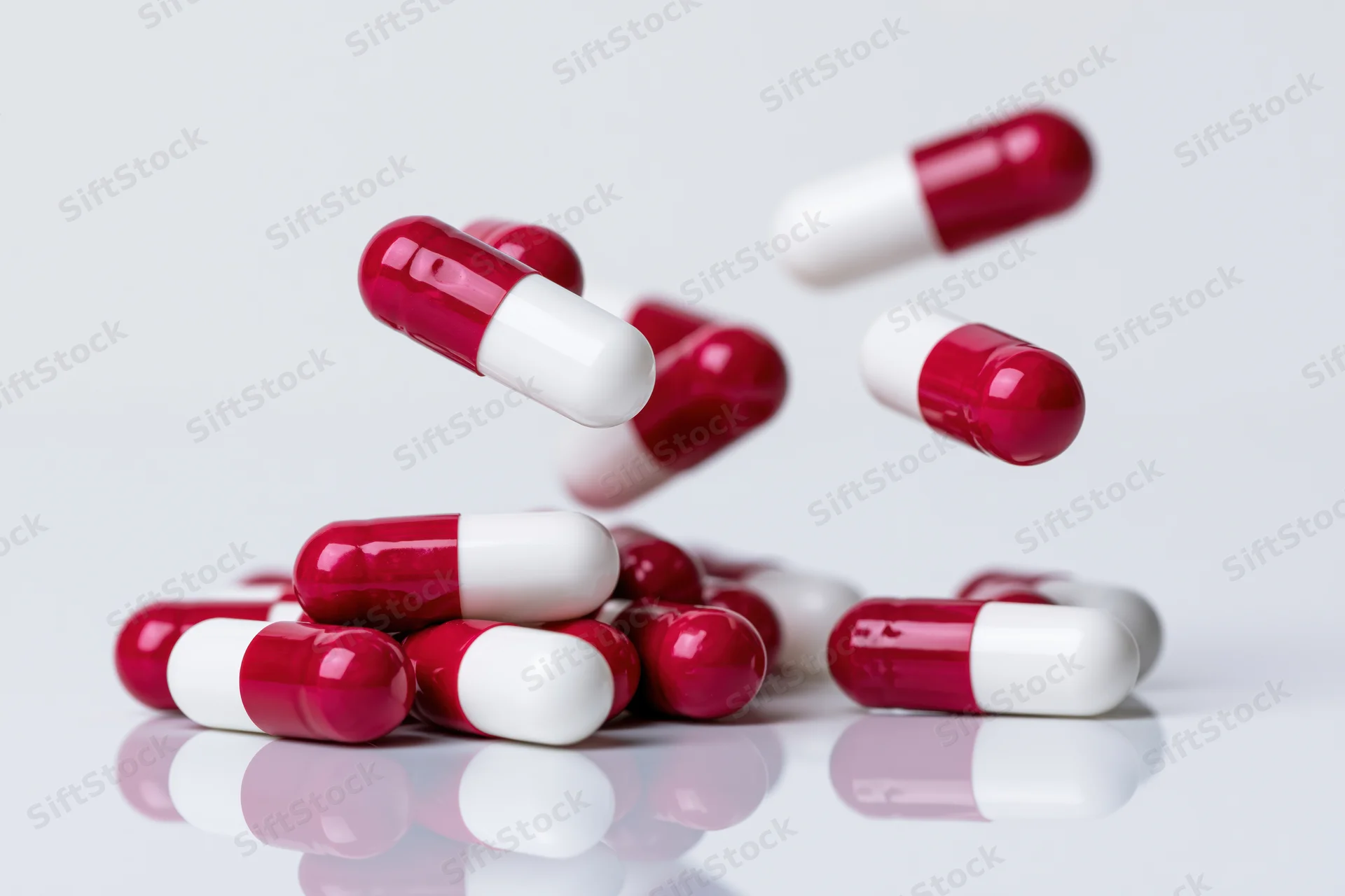 Red and white gelatin capsules falling and scattering on a reflective white surface