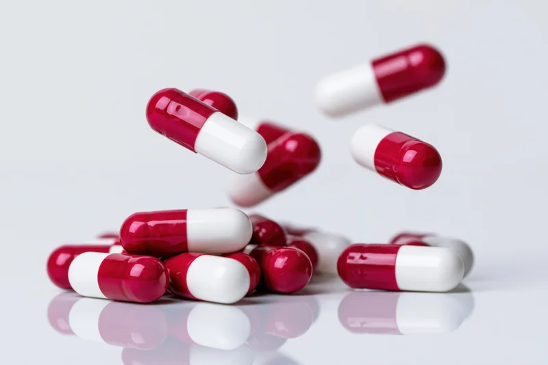 Red and white gelatin capsules falling and scattering on a reflective white surface