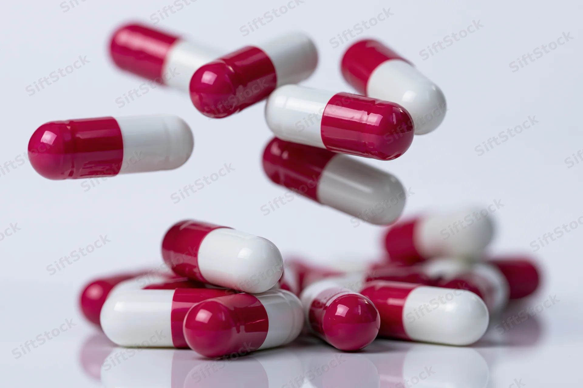 Red and white gelatin capsules falling and scattering on a reflective white surface