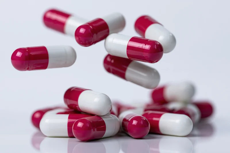 Red and white gelatin capsules falling and scattering on a reflective white surface